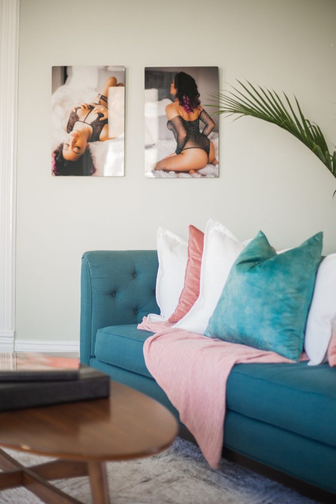 Teal couch with pillows next to a table with boudoir photography hanging on the wall