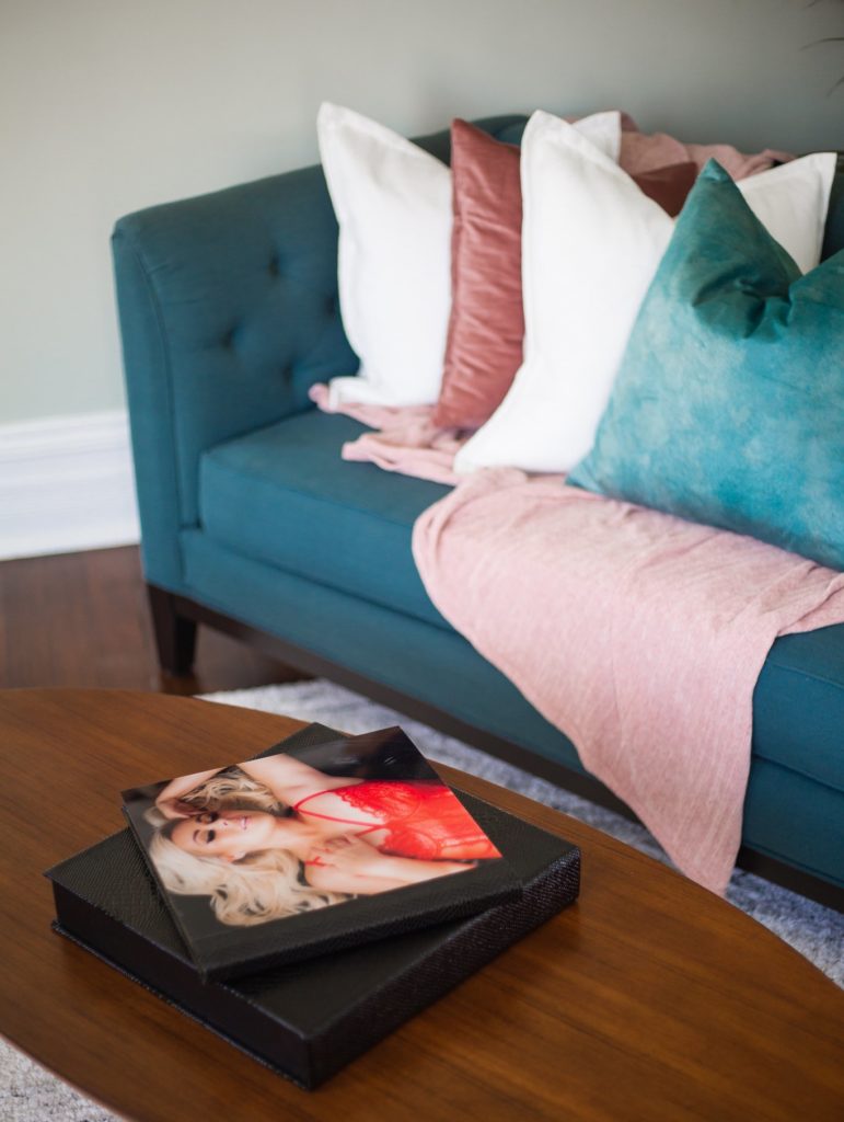 Teal couch with pillows next to a table with boudoir photography hanging on the wall